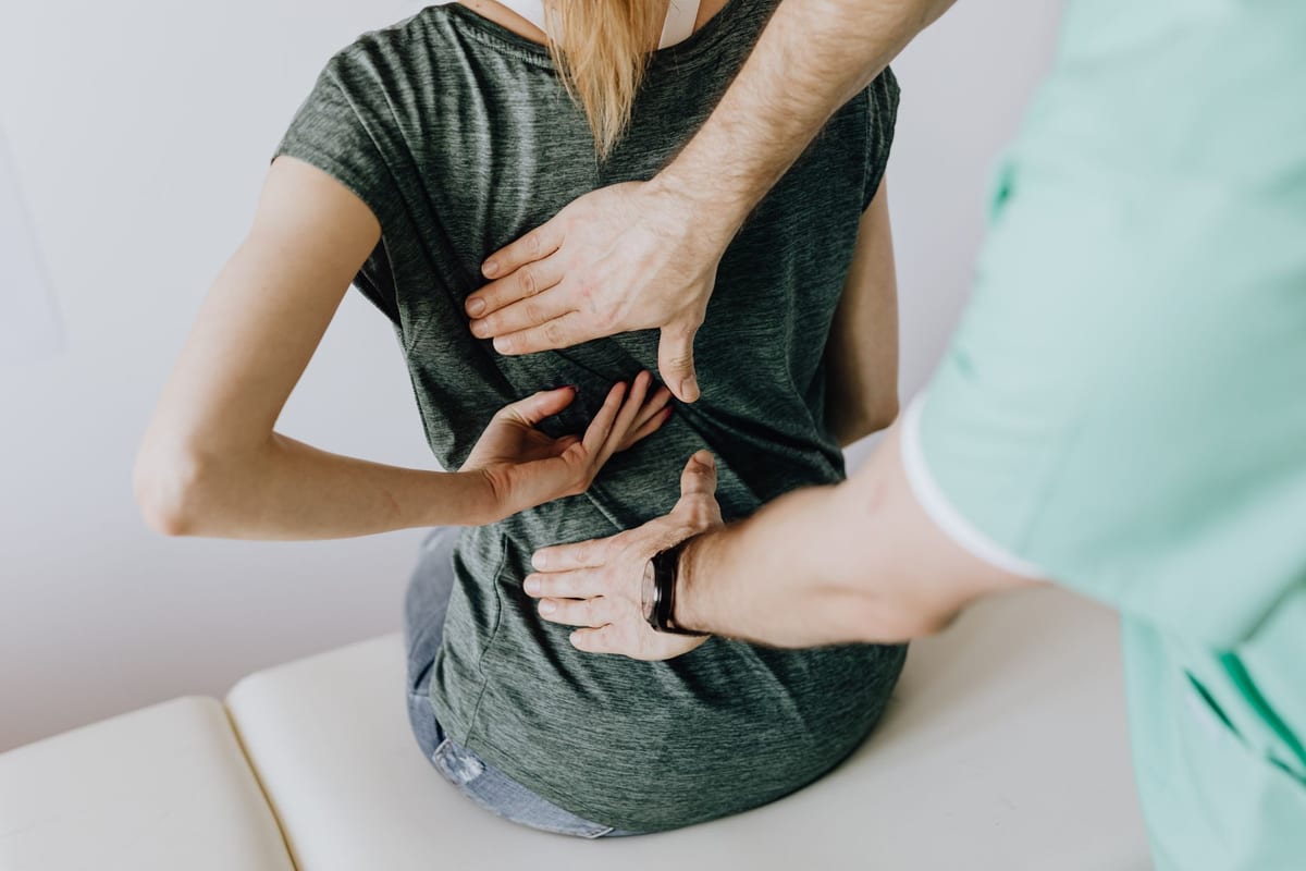 A clinician palpating a seated patient's lower back