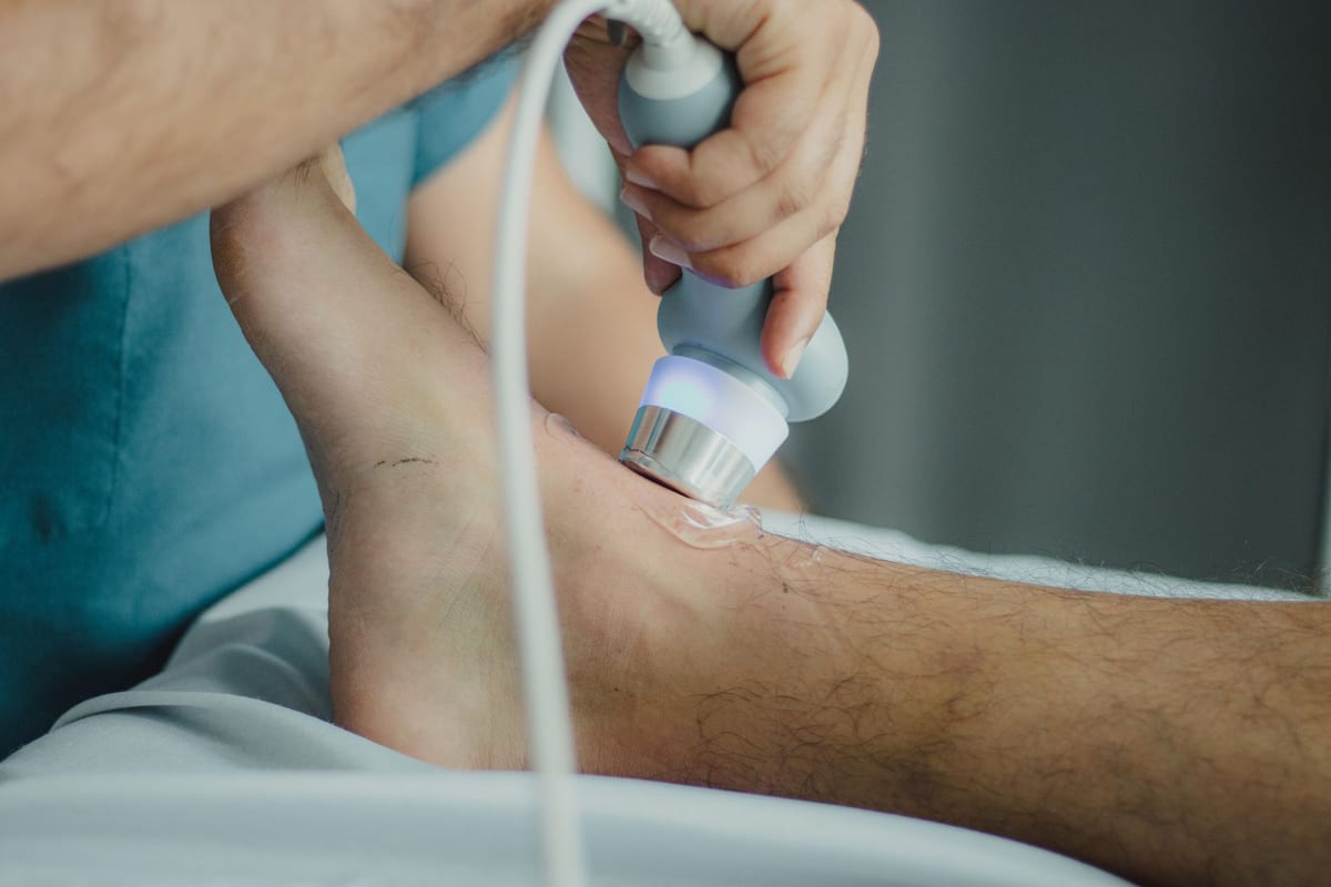 A therapeutic ultrasound head applied to a patient's ankle with gel